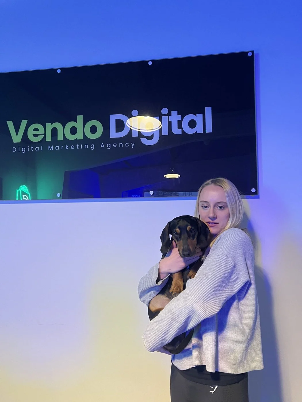 A Vendo team member holding the office dog beneath the Vendo Digital sign