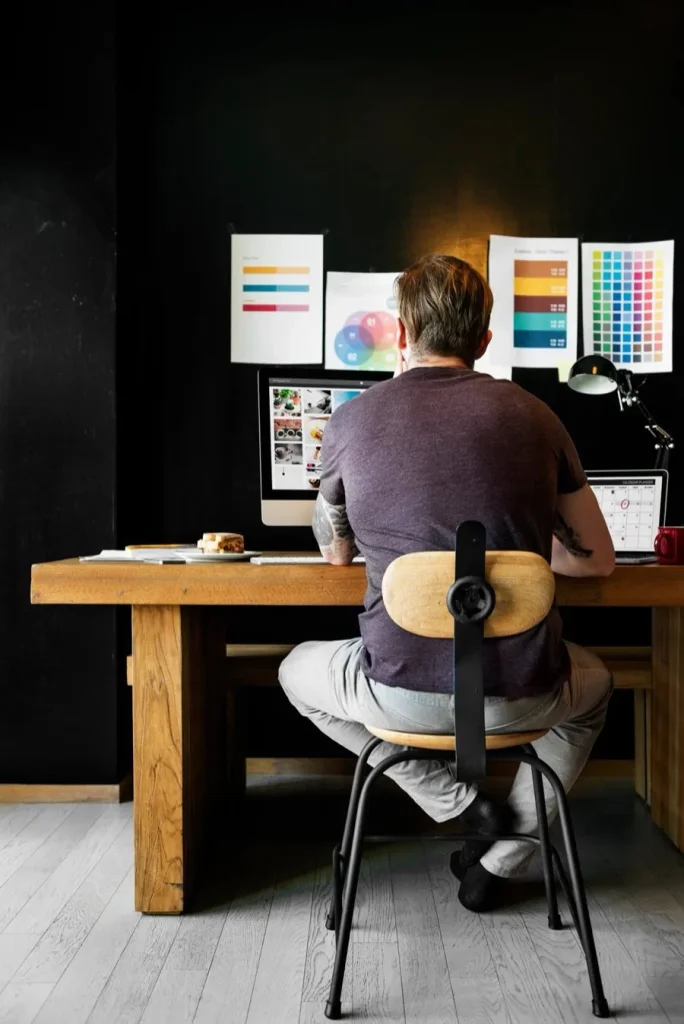 A designer at a wooden desk working on a website, with colour swatches pinned to the wall